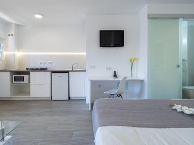 Chambre d'hôtel moderne avec kitchenette, lit et télévision murale.