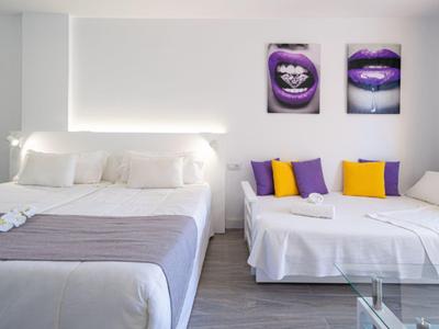 Chambre moderne avec grand lit, canapé-lit aux coussins colorés et décoration murale élégante.