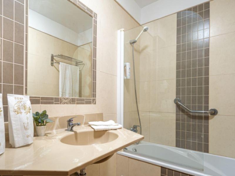 Salle de bain lumineuse avec lavabo, grand miroir et baignoire avec douche.
