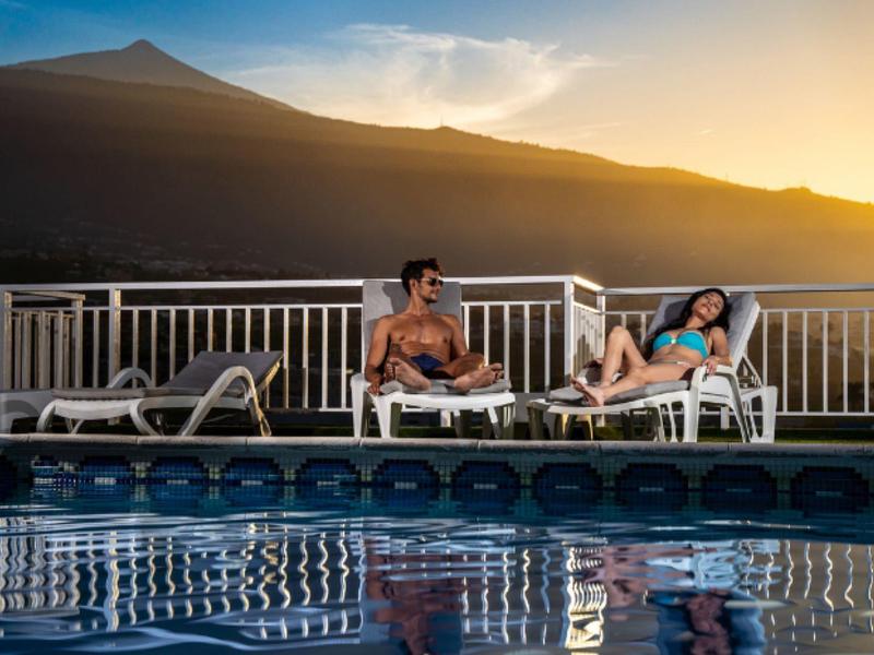 Deux personnes se détendent sur des chaises longues au bord d'une piscine au coucher du soleil en montagne.