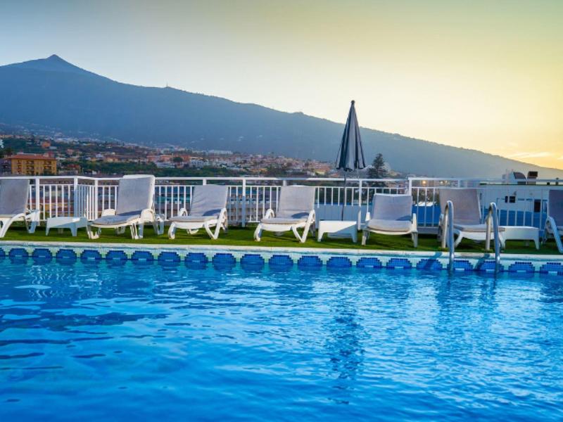 Piscine avec chaises longues et montagne en arrière-plan au coucher du soleil