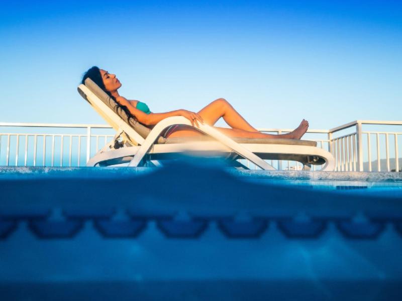 Femme se détend sur une chaise longue au bord de la piscine sous un ciel bleu clair