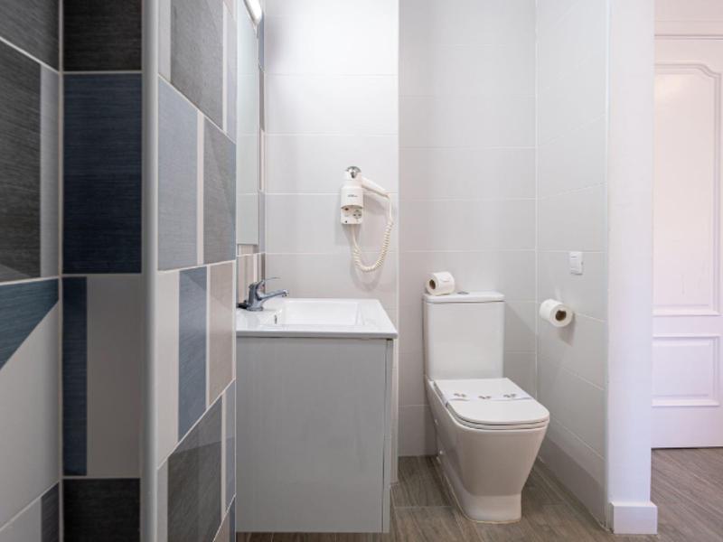 Salle de bain lumineuse avec toilettes blanches, lavabo et carreaux gris au mur.