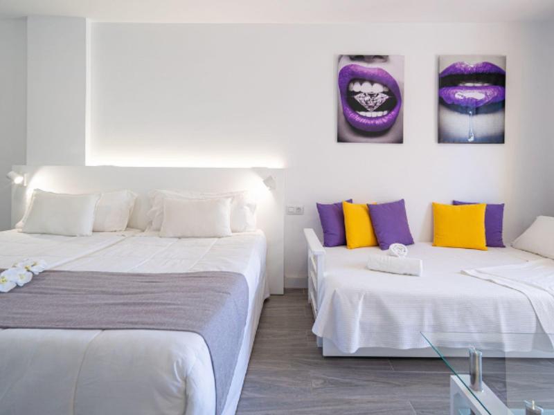 Chambre moderne avec grand lit, canapé-lit aux coussins colorés et décoration murale élégante.