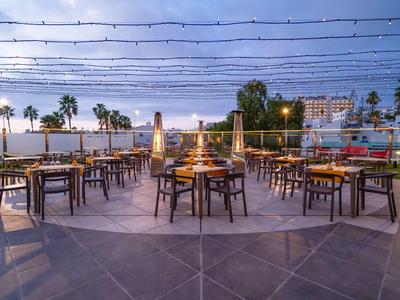 Area esterna moderna di un ristorante con sedie e tavoli in legno, illuminata al tramonto.