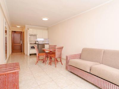 Soggiorno luminoso con divano, tavolo da pranzo e angolo cottura in un ambiente aperto.