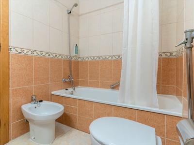 Piccolo bagno con vasca da bagno, tenda della doccia, bidet e WC con piastrelle marroni e bianche.