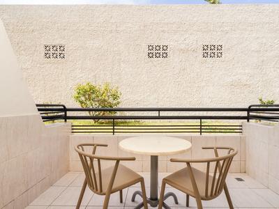 Balcone con tavolo rotondo e due sedie in legno con vista su un muro e vegetazione.