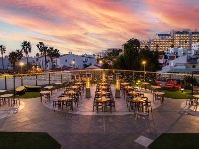 Ristorante all'aperto con tavoli e sedie vuoti sotto un cielo al tramonto colorato.