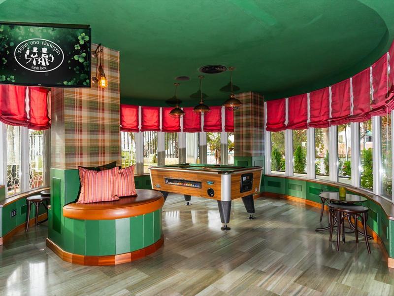 Area giochi elegante con tavolo da biliardo, nicchia colorata e tende rosse in un hotel.