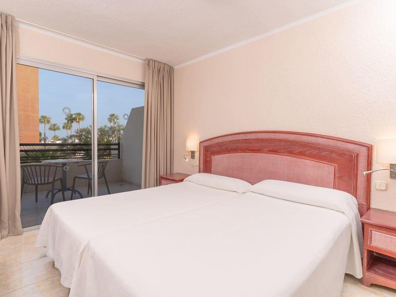 Camera d'hotel luminosa con letto matrimoniale e balcone con vista sugli alberi.