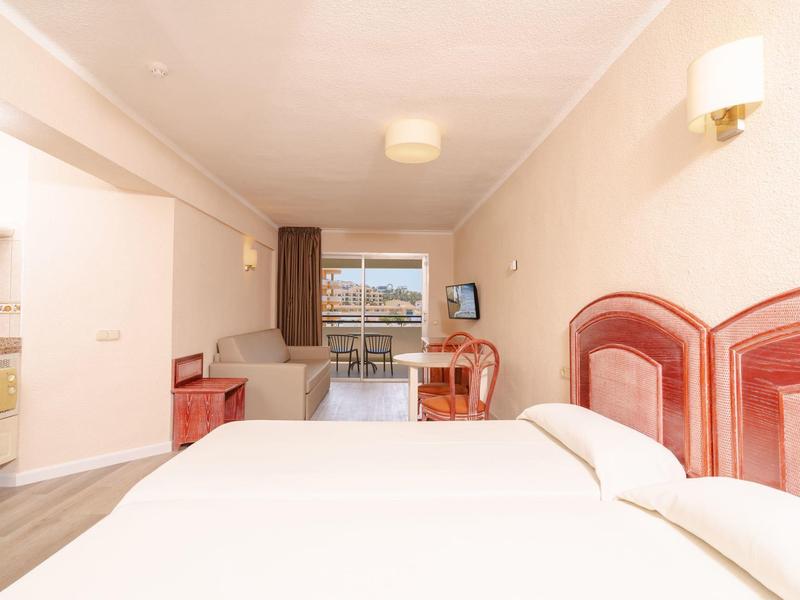 Camera d'albergo luminosa con due letti, scrivania e balcone con vista.