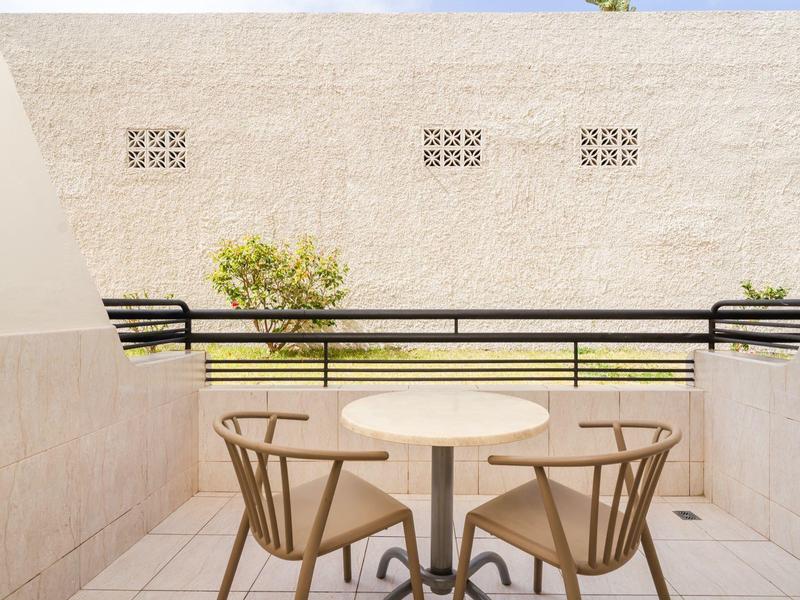 Balcone con tavolo rotondo e due sedie in legno con vista su un muro e vegetazione.