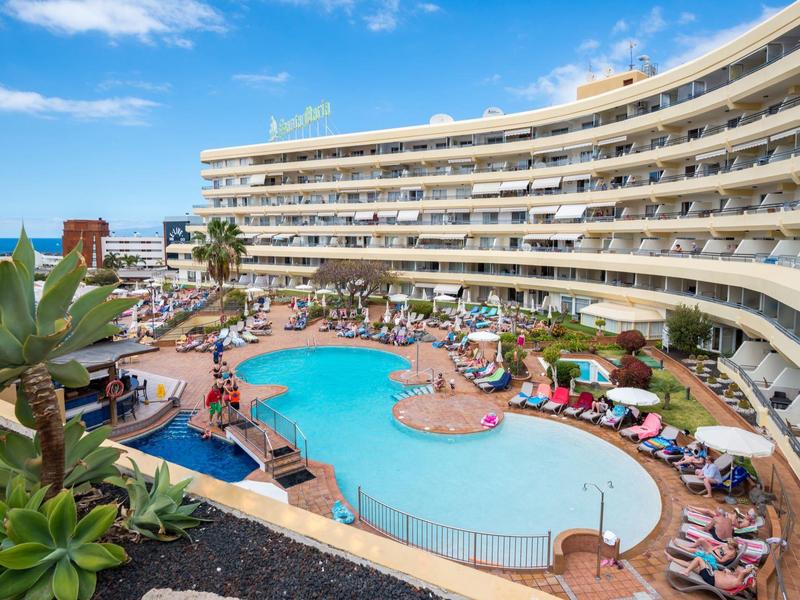 Grande hotel con piscina curva e sdraio, area esterna tropicale sotto cielo limpido.