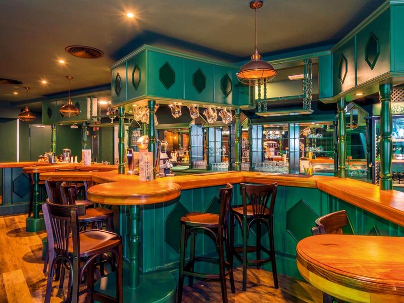 Accogliente bar dell'hotel con pannelli in legno verdi e illuminazione calda.