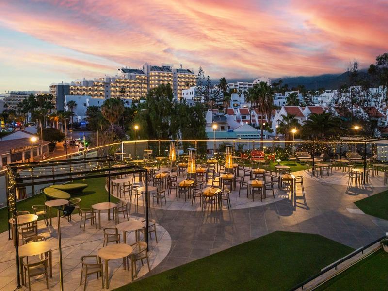 Terrazza esterna illuminata con tavoli e sedie al tramonto in un hotel.