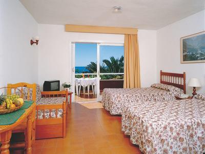 Helles Zimmer mit zwei Einzelbetten, großem Fenster, Holzmöbeln und Balkon mit Meerblick.