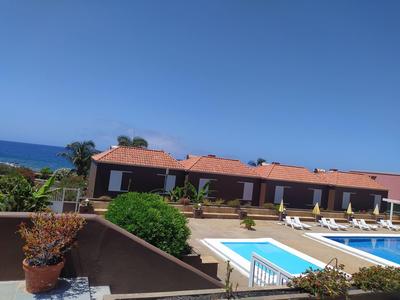 Mehrere braune Gebäude mit roten Dächern, Pool mit Liegestühlen und grünem Pflanzenbereich.