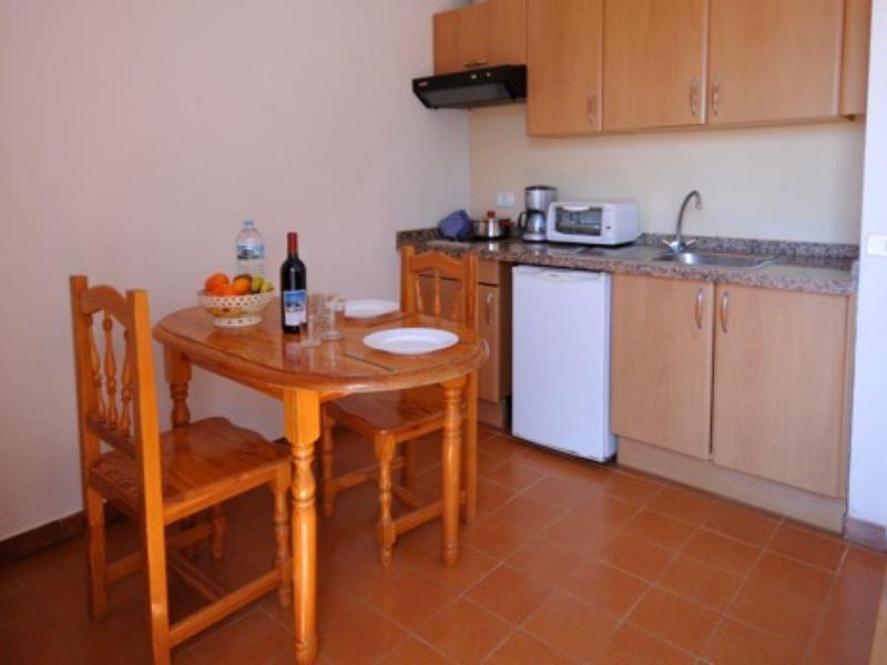 Kleine Küche mit Holzschränken, Tisch, zwei Stühlen und roten Fliesenboden.