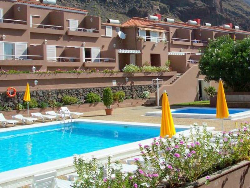 Hellblauer Pool mit gelben Sonnenschirmen und weißem Geländer vor mehrstöckigen braunen Gebäuden.