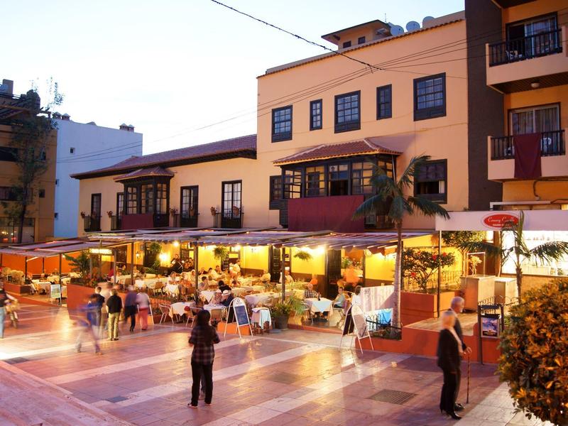 Abendliche Straßenszene mit beleuchteten Restaurants und Menschen, die an Tischen sitzen und gehen.