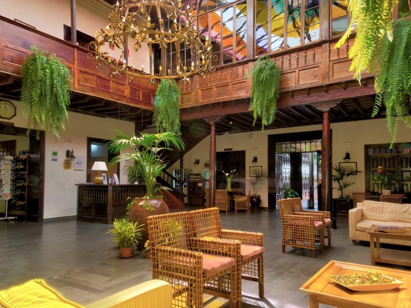 Gemütlicher Innenraum mit Holzmöbeln, hängenden Pflanzen und einem Kronleuchter unter Glasdach.