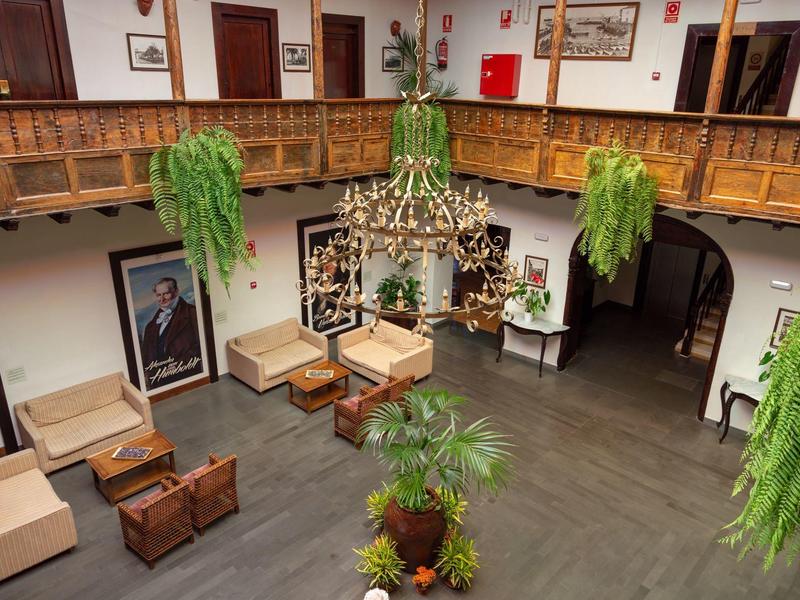 Großer Raum mit grauem Boden, hängenden grünen Pflanzen, Sitzgruppen und Holzgalerie oben.