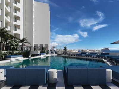 Nowoczesny basen hotelowy z niebieskimi leżakami i widokiem na morze pod błękitnym niebem.