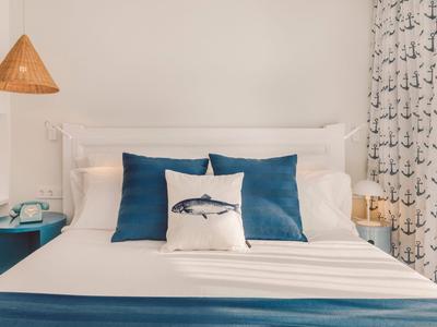 Nowoczesny pokój hotelowy z łóżkiem podwójnym, niebieskimi poduszkami i marynistyczną dekoracją.