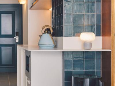 Kleine moderne Küchenecke mit blau gefliester Wand, beleuchtetem Lampenlicht und Hockern.