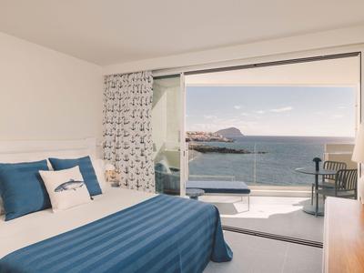 Sypialnia z niebieskim łóżkiem i widokiem na morze z balkonu.