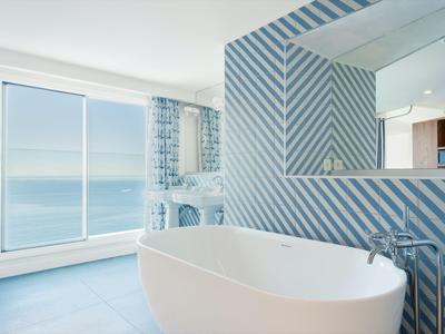 Bagno moderno con vasca autoportante e vista mare attraverso grandi finestre.