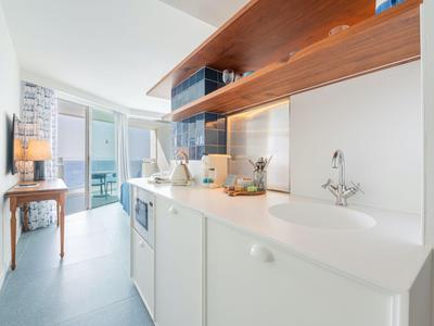 Cucina moderna in hotel con piano bianco, elementi in legno e balcone con vista mare.