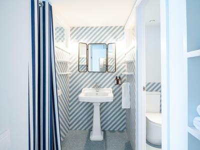 Bagno luminoso con lavabo, specchio e tenda doccia a righe.