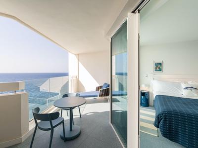 Balcone di una camera d'hotel con zona salotto e vista sul mare sotto un cielo limpido.