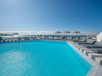 Piscina azzurra limpida con lettini e ombrelloni sotto un cielo limpido vicino al mare.