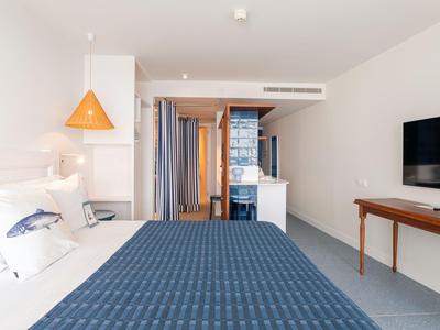 Camera d'hotel moderna con grande letto, TV e scrivania in tonalità neutre.