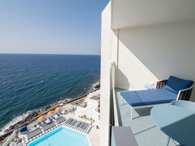 Balcone di un hotel con sedie e tavolo con vista sul mare e piscina.