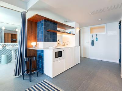 Area cucina moderna in una camera d'hotel con armadi bianchi e parete piastrellata blu.