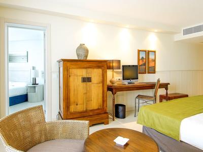 Jasny pokój hotelowy z drewnianymi meblami, zielonym narzutem i miejscem do siedzenia przy oknie.