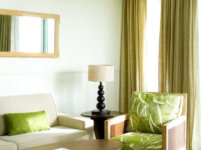 Jasny pokój hotelowy z zielonym fotelem, beżową kanapą, drewnianym stołem i zasłonami.