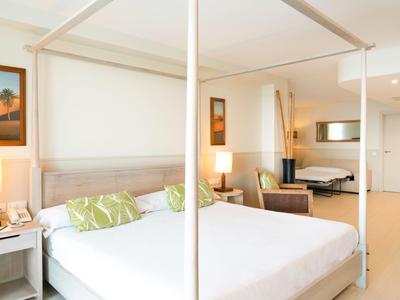 Jasny pokój hotelowy z dużym łóżkiem, białą pościelą i nowoczesnym wystrojem z ławką i lampami.