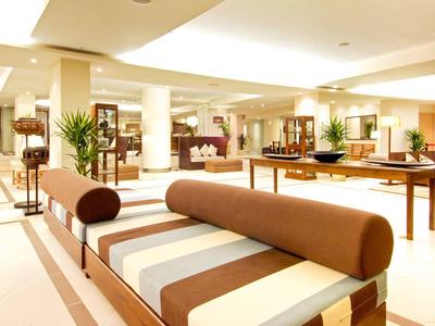 Jasny, przestronny hol hotelowy z nowoczesnymi beżowo-brązowymi siedziskami i dużymi roślinami.