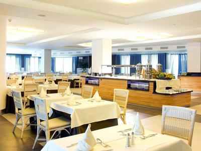 Jasna, przestronna jadalnia hotelowa z starannie ustawionymi stołami i bufetem.