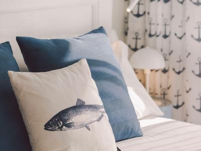 Hell dekoriertes Schlafzimmer mit weißen und blauen Kissen, Fischmotiv und Anker-Vorhängen.