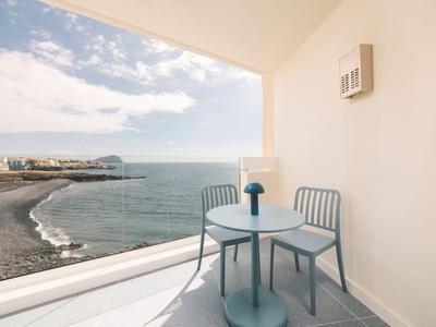 Balkon ze stołem i krzesłami z widokiem na morze i plażę pod niebieskim niebem.