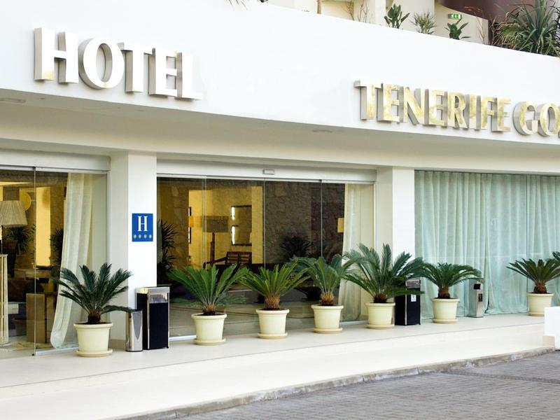 Wejście do hotelu z dużymi szklanymi drzwiami i kilkoma doniczkami z roślinami na zewnątrz.