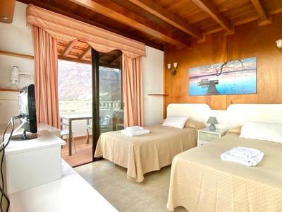 Hell eingerichtetes Hotelzimmer mit zwei Betten und Balkon mit Blick auf Berge.