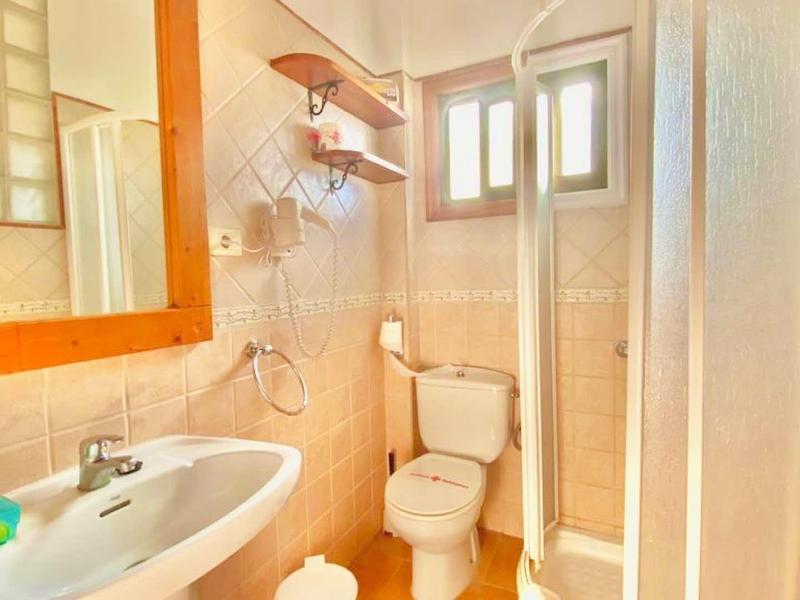Compact bathroom with sink, toilet, and shower cabin in warm tones.