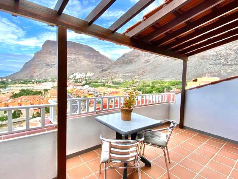 Large terrace with pergola, chairs, and view of mountains and town.